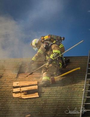 Fire fighter breaking through  roof shingles - with billowing smoke rising from the hole
